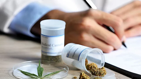 Arzt füllt Rezept aus, daneben Behältnisse mit medizinischem Cannabis