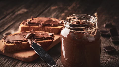 Glas mit Schokoladencreme, daneben Brote mit Schokoaufstrich