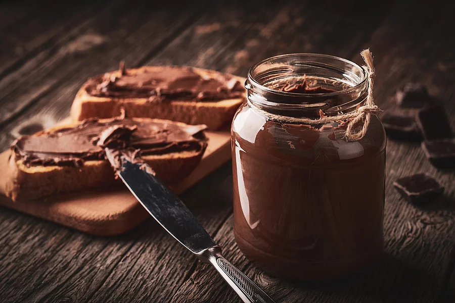 Glas mit Schokoladencreme, daneben Brote mit Schokoaufstrich