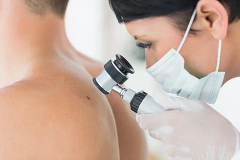 Dermatologin untersucht Haut eines Patienten mit Lupe