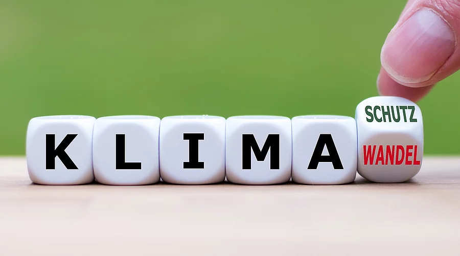 Symbol für mehr Klimaschutz: Hand dreht einen Würfel und änder das Wort "Klimawandel" in "Klimaschutz". Würfel mit der Aufschrift "Klima"