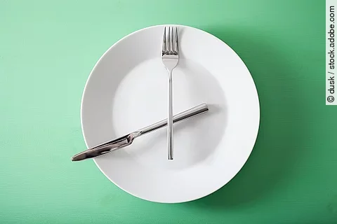 Intervallfasten, leerer Teller mit Besteck als Uhrzeiger 