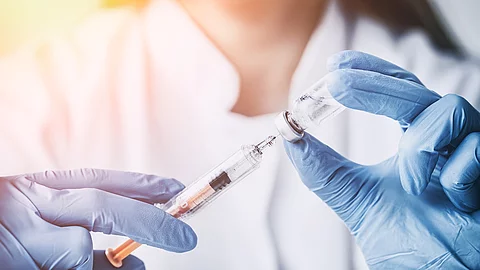 Eine Ärztin mit blauen Handschuhen zieht eine Impfung auf. Eine Ärztin mit blauen Handschuhen zieht eine Impfung auf.
