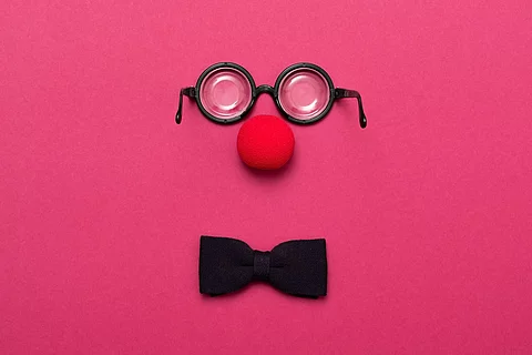 Eine Brille, eine rote Clownsnase und eine Schleife auf pinkem Hintergrund.