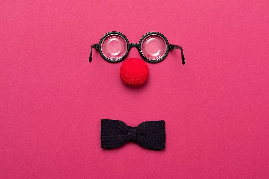 Eine Brille, eine rote Clownsnase und eine Schleife auf pinkem Hintergrund.