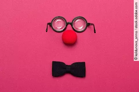 Eine Brille, eine rote Clownsnase und eine Schleife auf pinkem Hintergrund.