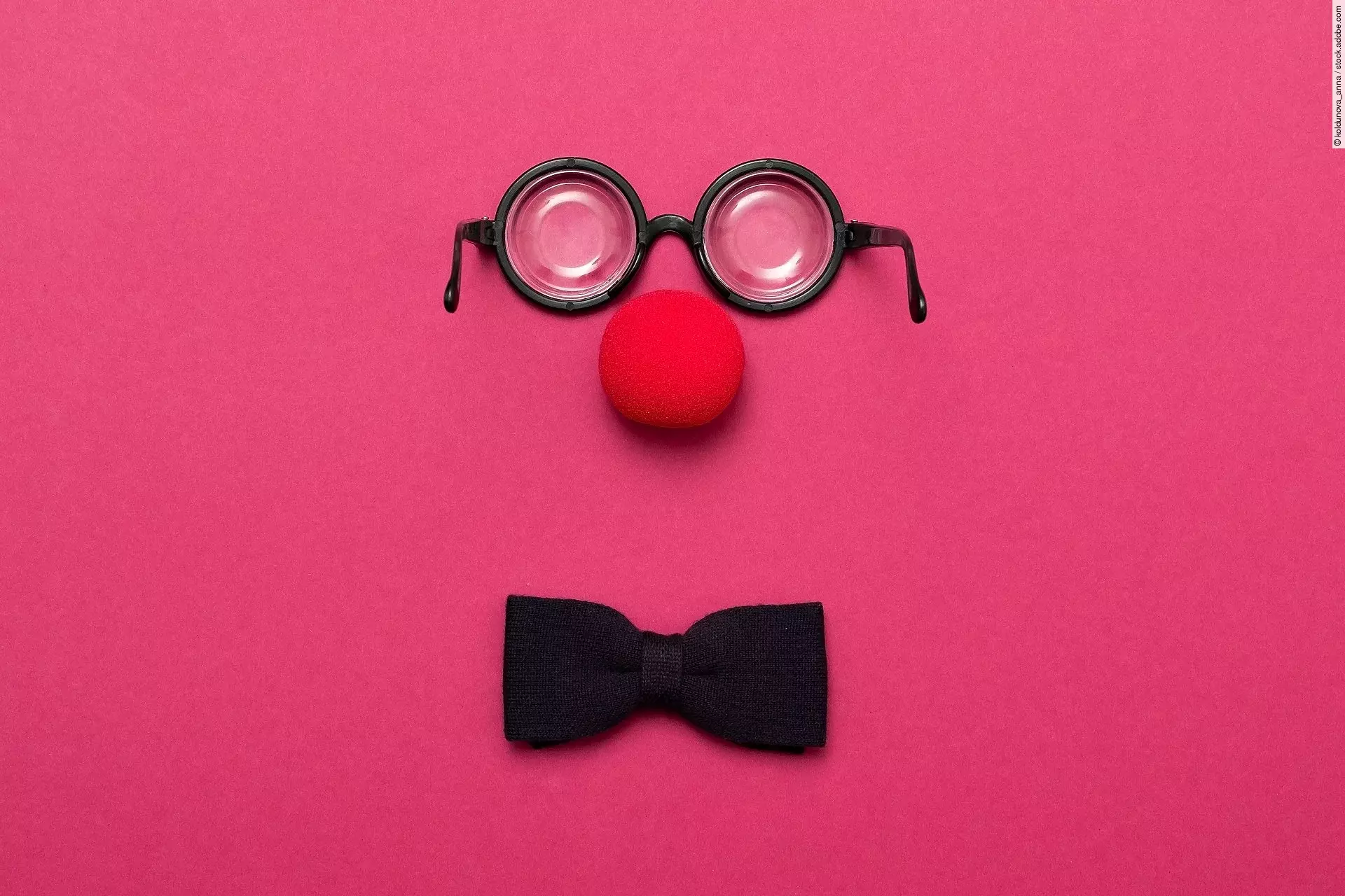 Eine Brille, eine rote Clownsnase und eine Schleife auf pinkem Hintergrund.