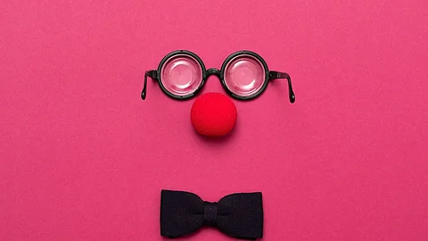 Eine Brille, eine rote Clownsnase und eine Schleife auf pinkem Hintergrund.