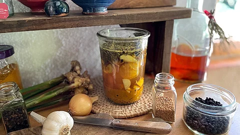 Zutaten für Fire Cider auf Küchenarbeitsplatte: Knoblauch, Weckglas mit Apfelessig, Pfefferkörner, Zwiebel, Holzbrett mit Messer