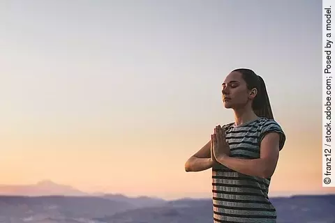jubge Frau praktiziert Sonnengebet im Sonnenuntergang