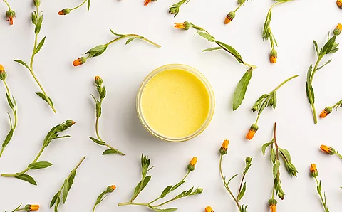 Glas mit gelber Salbe gefüllt; Daneben getrocknete Ringelblumen