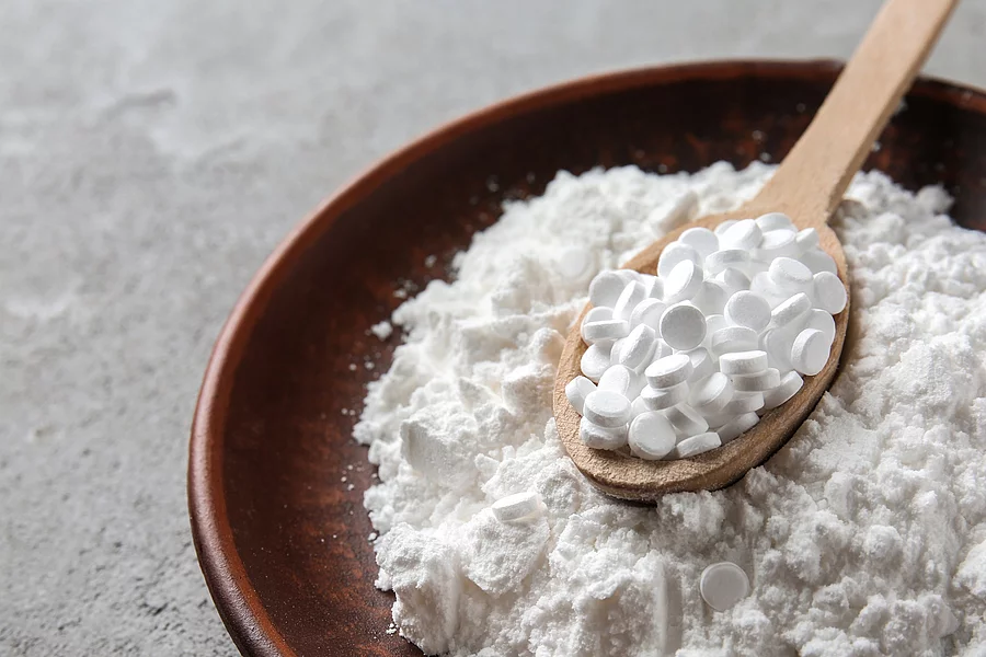 Puderzucker in einer Holzschale, darauf ein Holzlöffel mit Süßstofftabletten