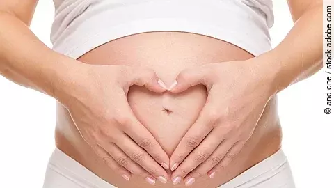 Schwangere hält ihren Bauch und bildet eine Herzform mit den Händen.