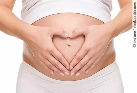 Schwangere hält ihren Bauch und bildet eine Herzform mit den Händen.