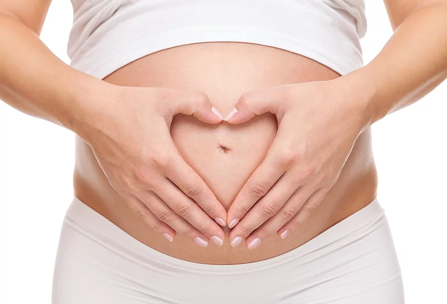 Schwangere hält ihren Bauch und bildet eine Herzform mit den Händen.