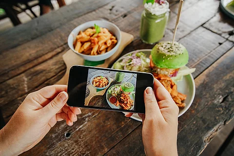 Frauenhand fotografiert Essen auf Holztisch
