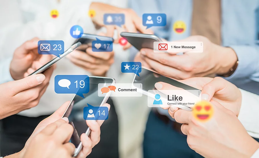 5 Hände tippen auf Handys. Darüber Sprechblasen mit Symbolen für Likes, Shares, Daumen hoch