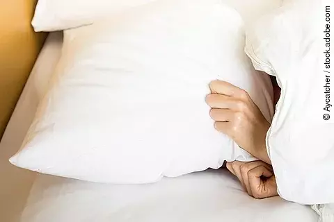 Person liegt im Bett, nur Hände sind zu sehen, die nach dem Kissen greifen.