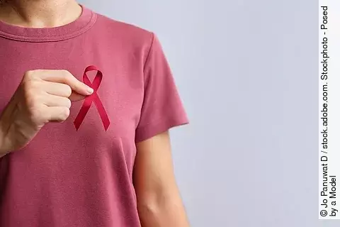 Frau im rosa T-Shirt hält rote Krebsschleife