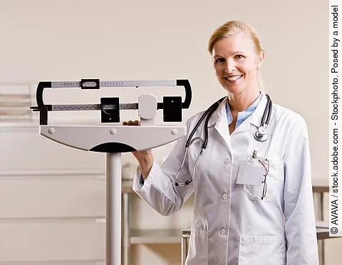 Arzt steht neben einer Waage.