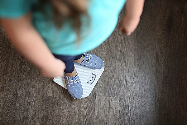Overweight girl standing on floor scales indoors Übergewichtiges Kind, das auf der Waage steht.