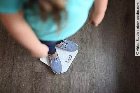 Übergewichtiges Kind, das auf der Waage steht.