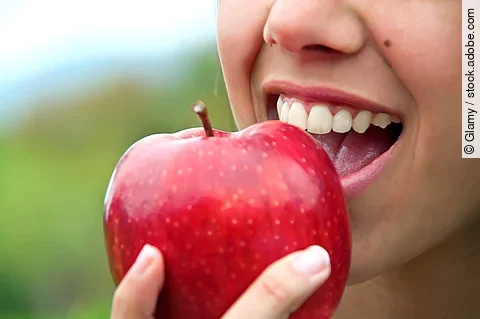 Frau mit gesunden weißen Zähnen beißt in einen Apfel