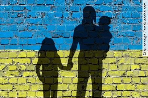 Flucht: Frauen und Kinder auf der Flucht; als Schatten vor einer Mauer in Ukrainefarben