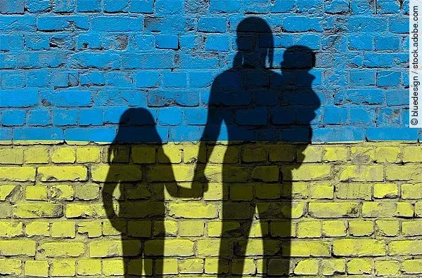Flucht: Frauen und Kinder auf der Flucht; als Schatten vor einer Mauer in Ukrainefarben