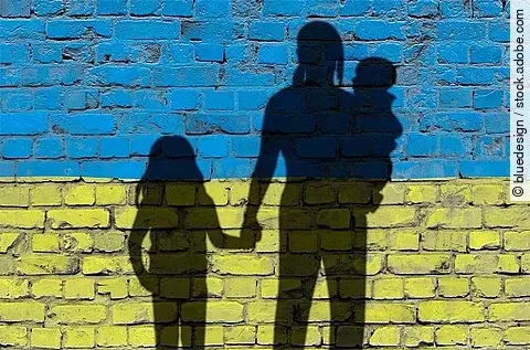 Flucht: Frauen und Kinder auf der Flucht; als Schatten vor einer Mauer in Ukrainefarben