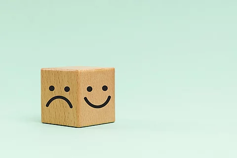 Holzwürfel mit einem lachenden und traurigen Smiley auf türkisem Hintergrund.