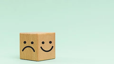 Holzwürfel mit einem lachenden und traurigen Smiley auf türkisem Hintergrund.