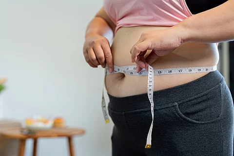 Übergewichtige Frau misst ihren Bauchumfang mit einem Maßband