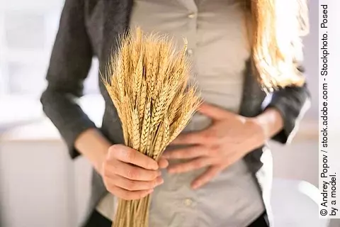 Eine Frau hält sich mit einer Hand den Bauch, in der anderen Hand hält sie ein Büschel Weizen.