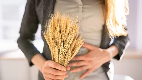 Eine Frau hält sich mit einer Hand den Bauch, in der anderen Hand hält sie ein Büschel Weizen.