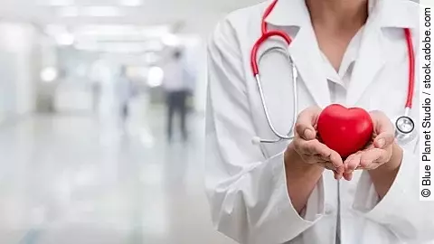 Ein Arzt hält eine rote Herzfigur in den Händen 