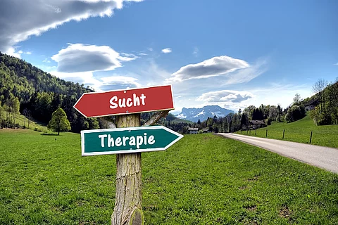 2 Wegweiser vor Berglandschaft: links: Sucht, rechts: Therapie