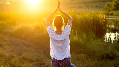 Frau in Yogapose auf einer Wiese im Sonnenuntergang