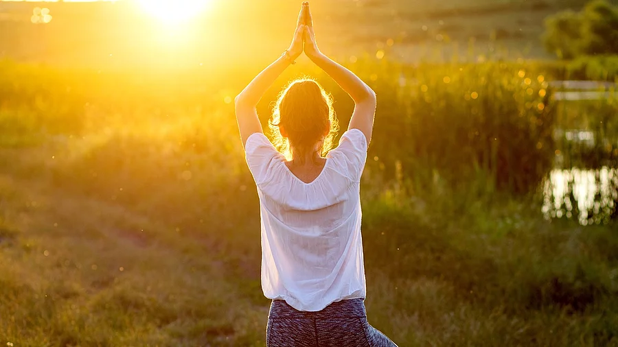 Frau in Yogapose auf einer Wiese im Sonnenuntergang