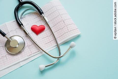 Stethoskop und Herzfigur liegen auf einem Kardiogramm. 