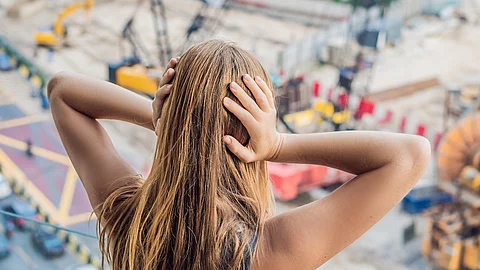 Junge Frau am Fenster blickt auf die Straße und hält sich die Ohren zu