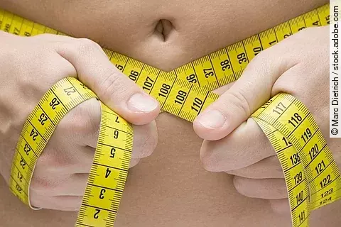 Person misst ihren Bauchumfang mit einem Maßband.