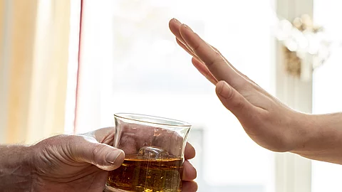 Eine Hand hält ein Glas mit Whisky, eine zweite Hand wehrt das Glas ab