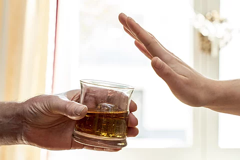 Eine Hand hält ein Glas mit Whisky, eine zweite Hand wehrt das Glas ab