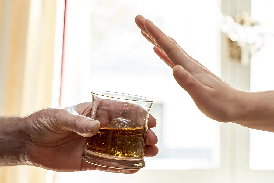 Eine Hand hält ein Glas mit Whisky, eine zweite Hand wehrt das Glas ab