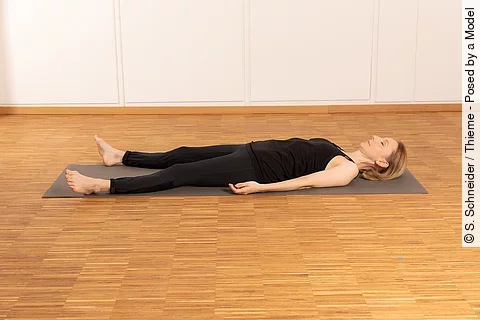 Frau in schwarze Sportsachen liegt auf Holzboden in Rücken-Entspannungslage