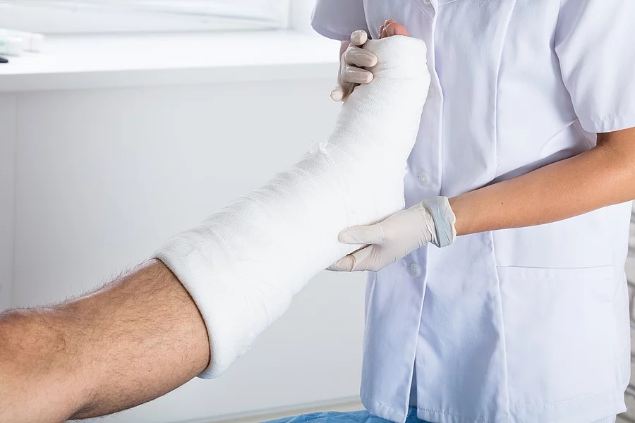 Arzt untersucht eingegipstes Bein eines Patienten.