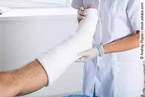 Arzt untersucht eingegipstes Bein eines Patienten. 