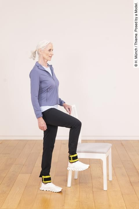 Frau in Sportkleidung macht eine Übung neben einem weißen Stuhl.