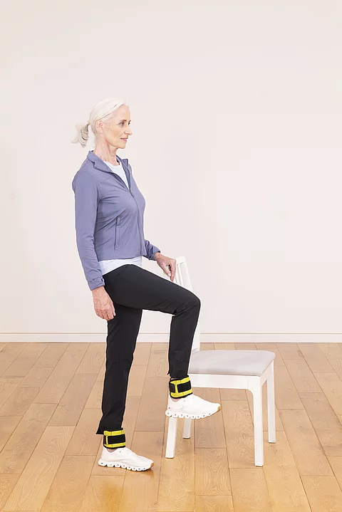 Frau in Sportkleidung macht eine Übung neben einem weißen Stuhl.